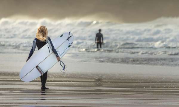 woman walking into surf with surfboard